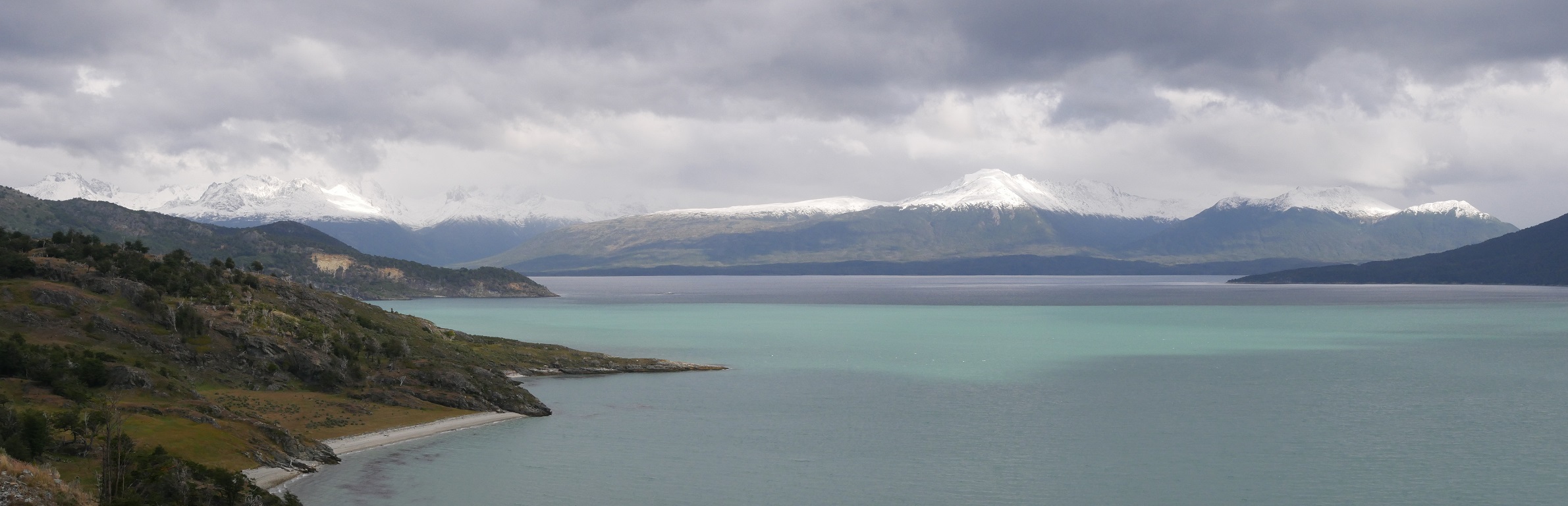 Blick aus der Bahía Yendegaia nach Süden auf den Beagle Kanal und die gegenüberliegende Insel Hoste. Das grüne Gletscherwasser des Rio Yendegaia mischt sich mit dem dunkleren Meerwasser; in den Hochlagen hat es geschneit.